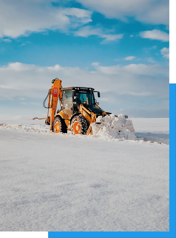 Commercial Snow Removal & Ice Control 1 Backhoe Loader Plowing Snow Under Clear Sky / Alt: Orange backhoe loader pushing snow across an open field under a blue sky