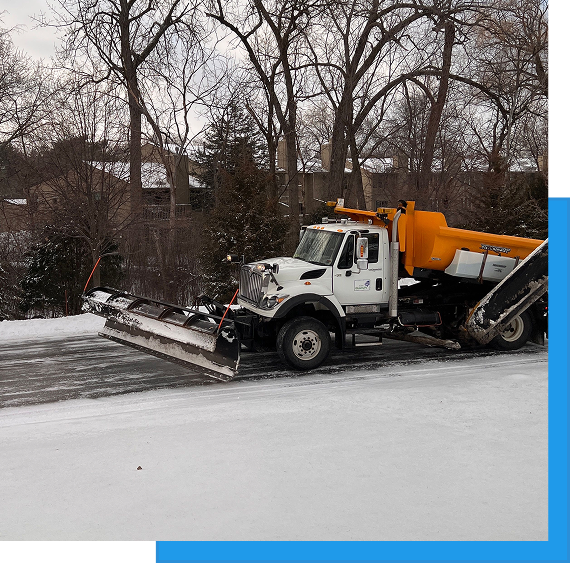Commercial Snow Removal & Ice Control 3 White snow plow truck with attached blade clearing a snowy walkway near trees