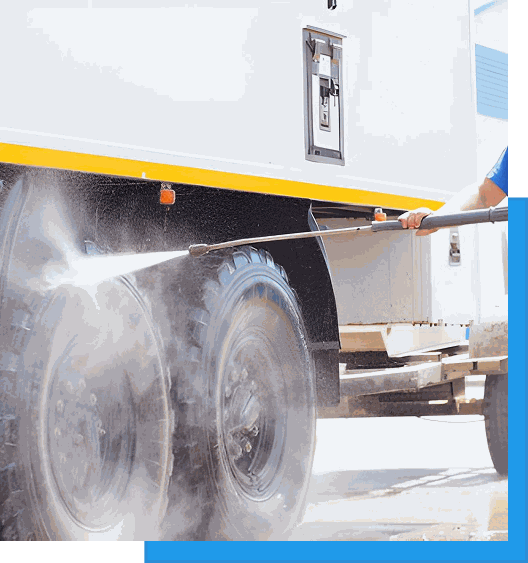 Worker pressure washing the wheels and undercarriage of a white semi-truck trailer