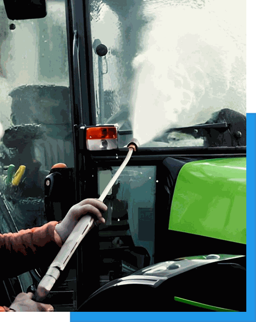 Worker pressure washing the cab and windows of a green tractor