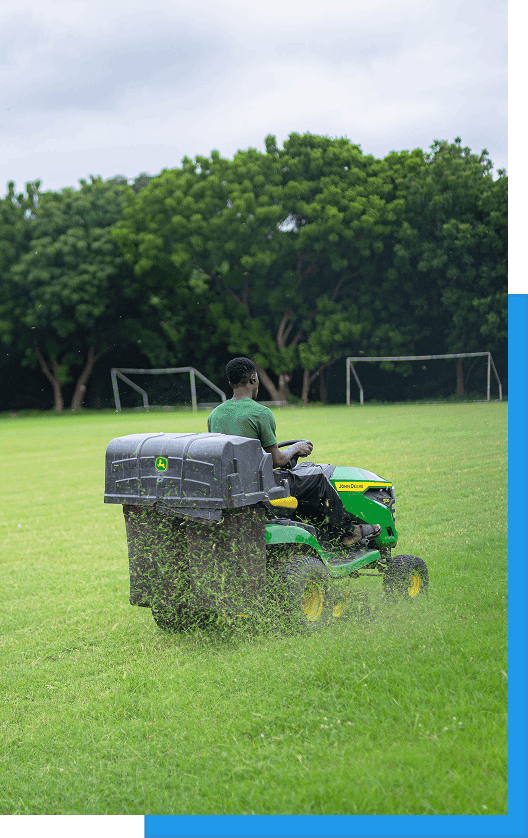 Operator mowing a sports field with a riding mower and grass bagger attachment